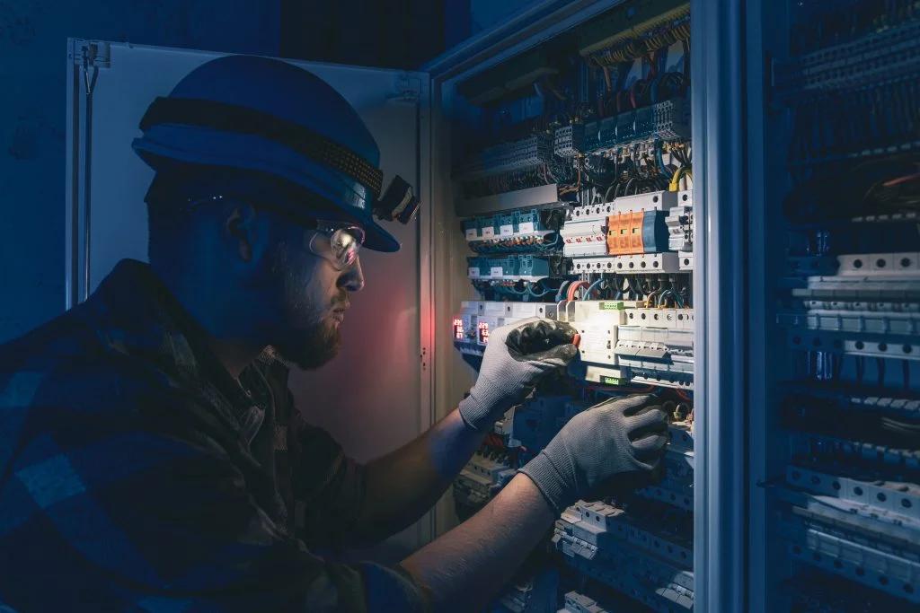 Electrician in a hard hat working on a large electrical panel in dramatic low light