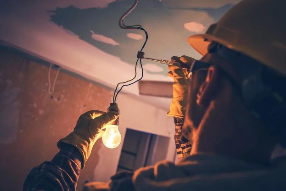 Electrician installing a ceiling light, bulb glowing warmly in a dark room