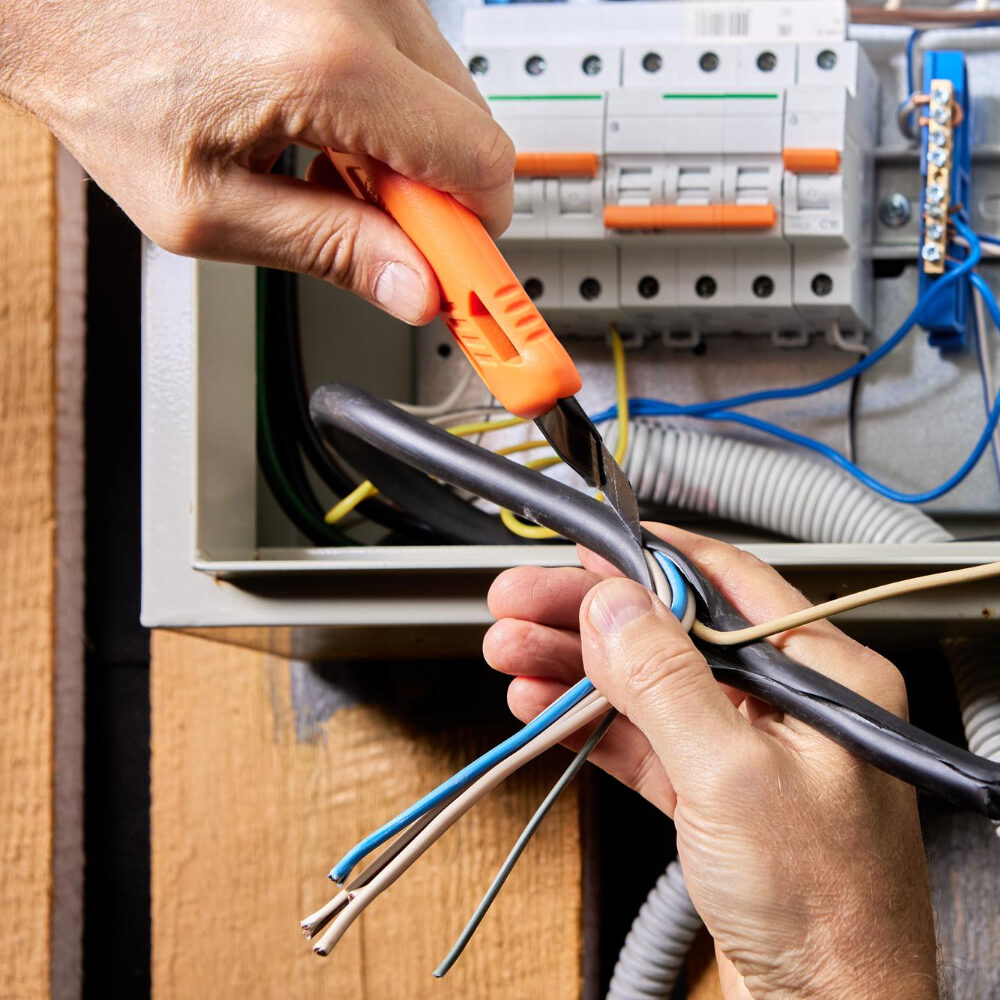 Close-up of hands stripping and preparing electrical wiring at a breaker box